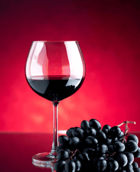 Verre de vin rouge et grappe de raisin sur fond rouge.