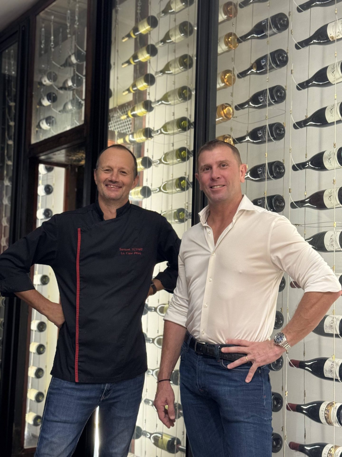 Deux hommes posant devant une cave à vin moderne.